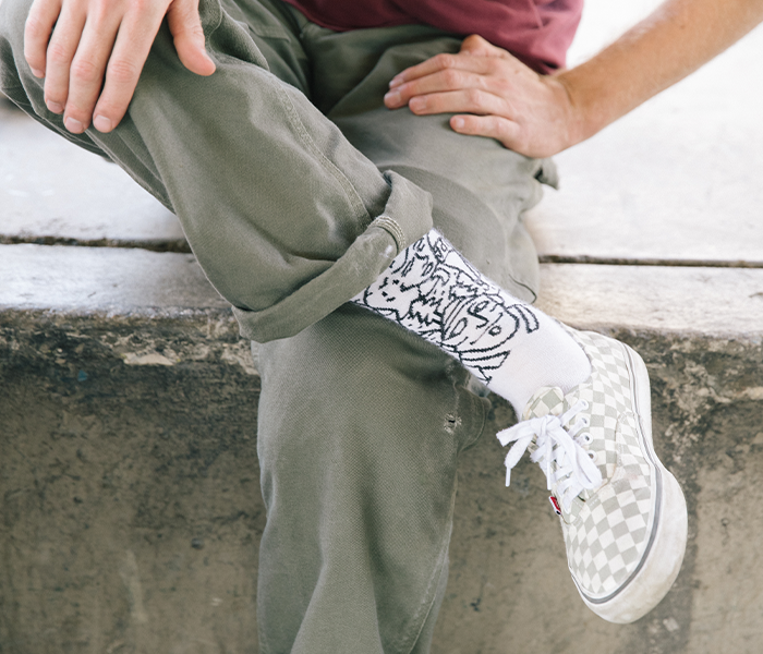 A cross-legged fellow sitting on a concrete ledge while wearing unique socks with Vermont inspired graphics 