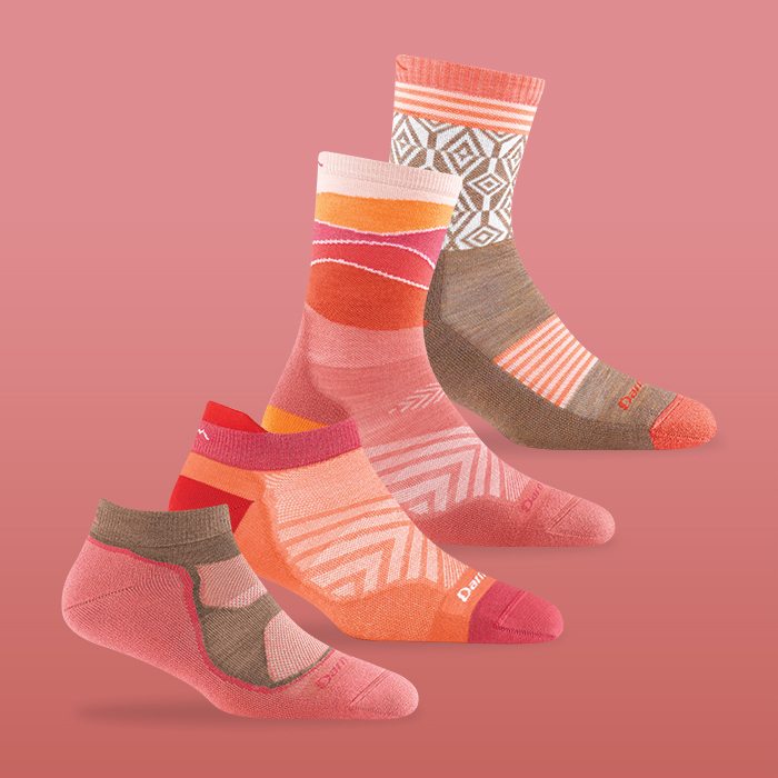 Shop Coral Socks - four coral-colored Darn Tough socks lined up against a coral background.