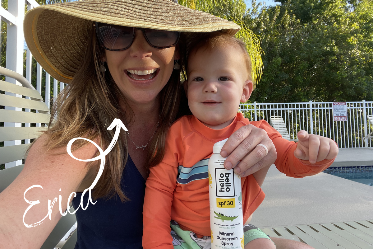 Hip2Save's Erica with her baby smiling at the pool while holding a Hello Bello SPF 30 Mineral Sunscreen Spray
