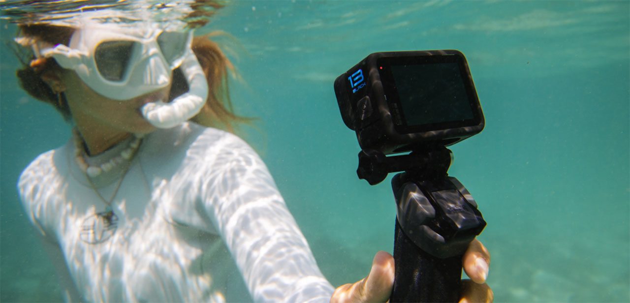 A man swimming in the ocean with fish while holding a GoPro camera.