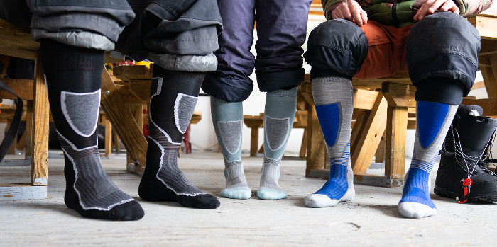 a line up of three people all wearing the wonderful Outer Limits ski/ride sock from Darn Tough. They are standing in a rustic lodge setting, but you just see their feet. It's super clever.