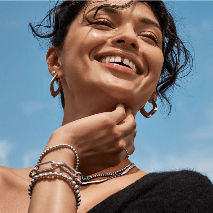 A smiling woman happily showcases her new gold & silver necklaces and bracelets, as well as beautiful earrings.