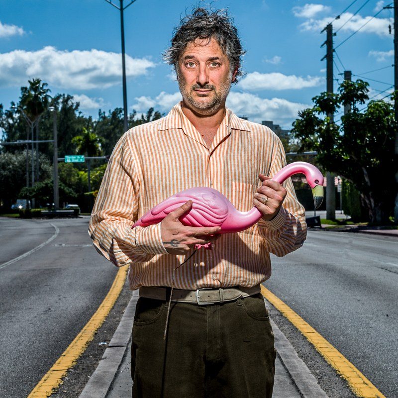 harmony korine stand in the middle of the road holding a pink lawn flamingo
