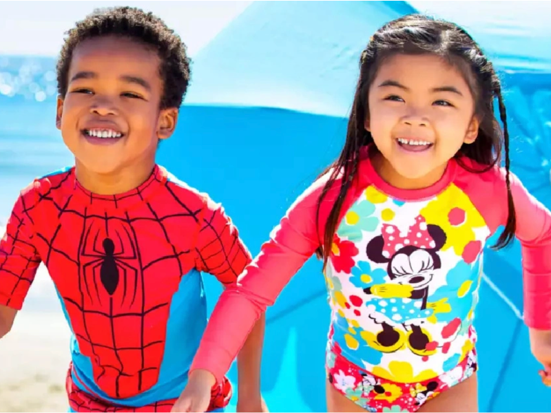 Two children wearing Disney Swimsuits in Spiderman and Minnie Mouse on a beach