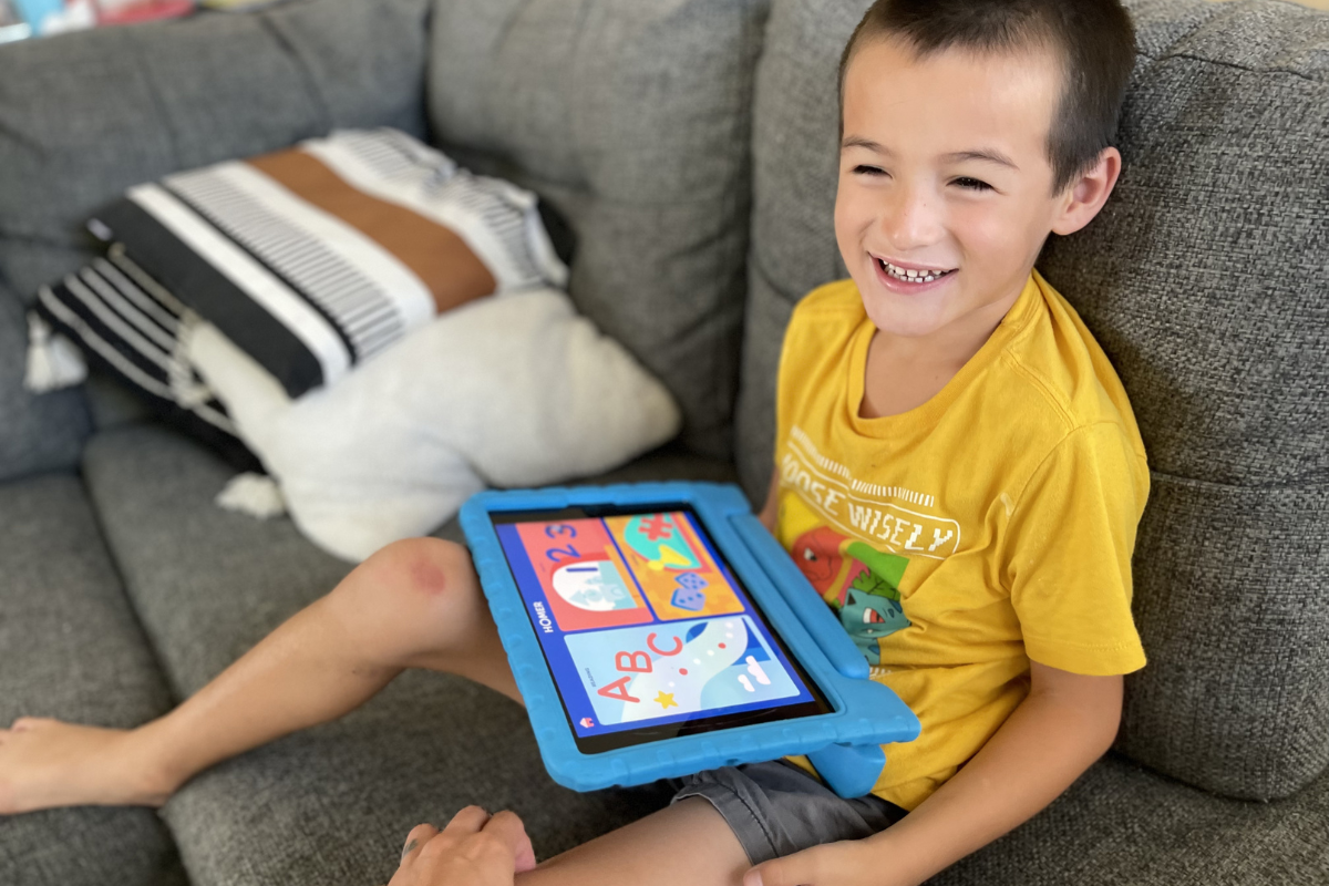 Child sitting on a couch with a blue tablet set to Homer Early Learning Program app