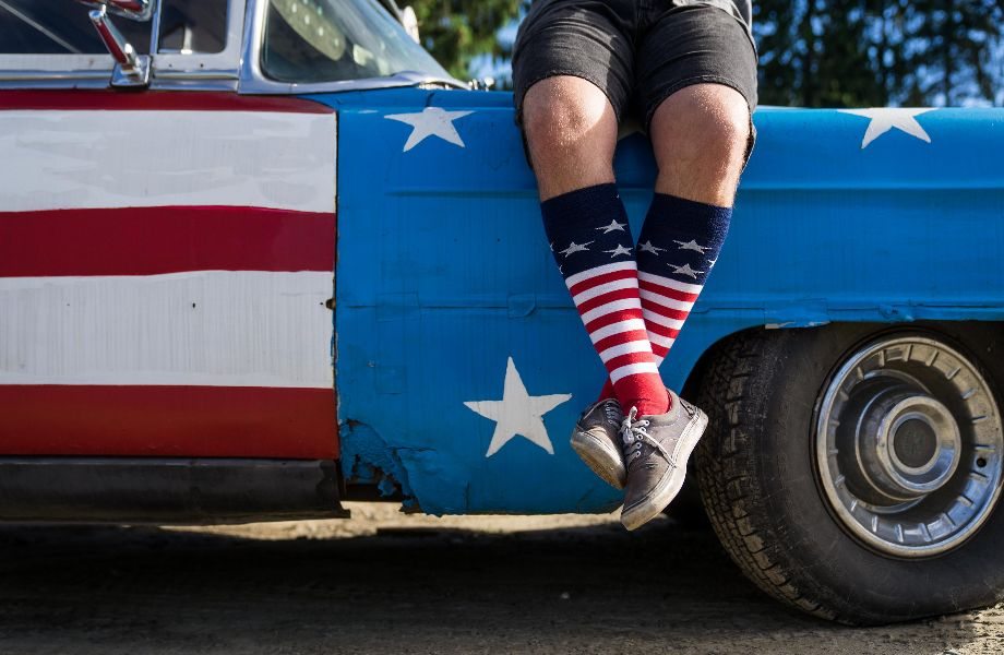 A very cool American sits on a USA flag-painted truck, ankles crossed, calves covered completely in stars and striped socks. 