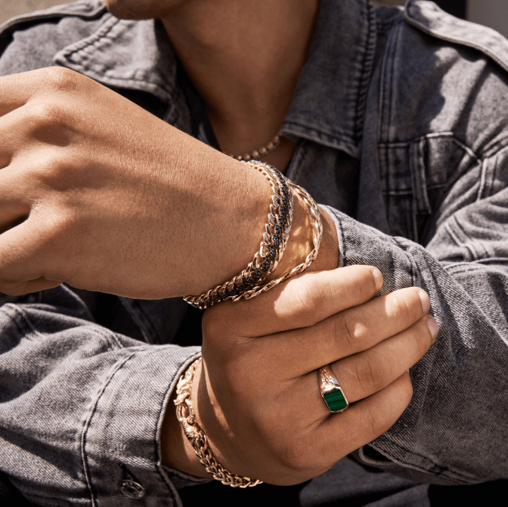 A man showcasing a stylish chain bracelet and a ring on his hand, emphasizing his fashionable accessories.