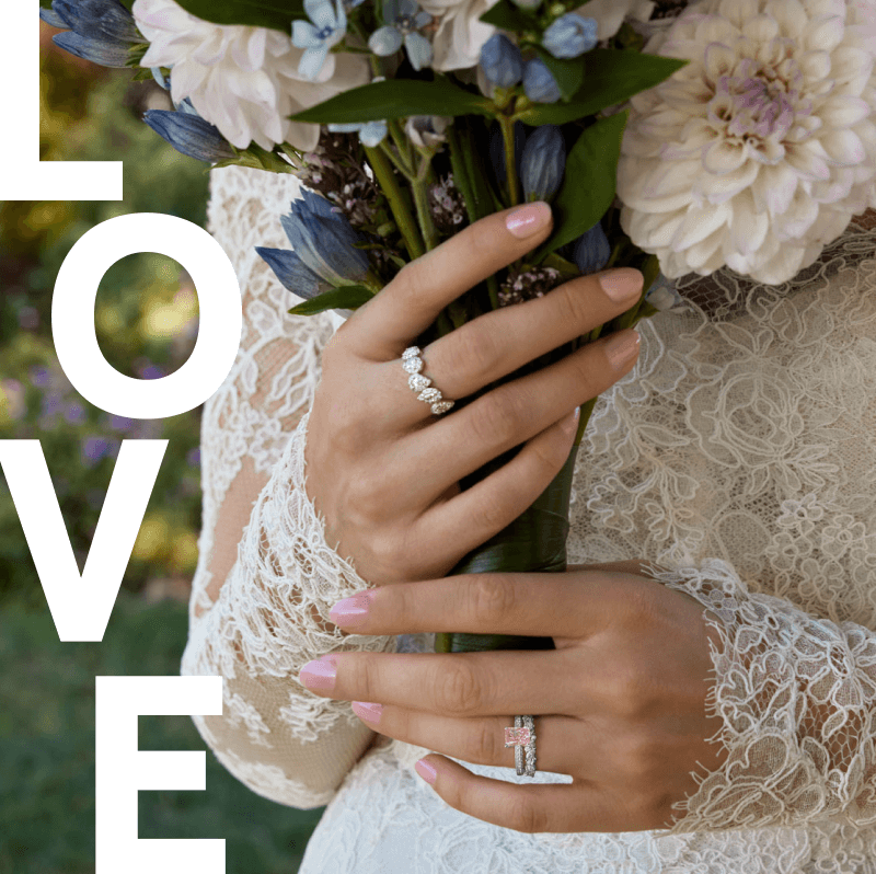 A woman with beautiful wedding rings on her hands holding a vibrant bouquet of flowers, surrounded by the word ''love'' in elegant lettering.