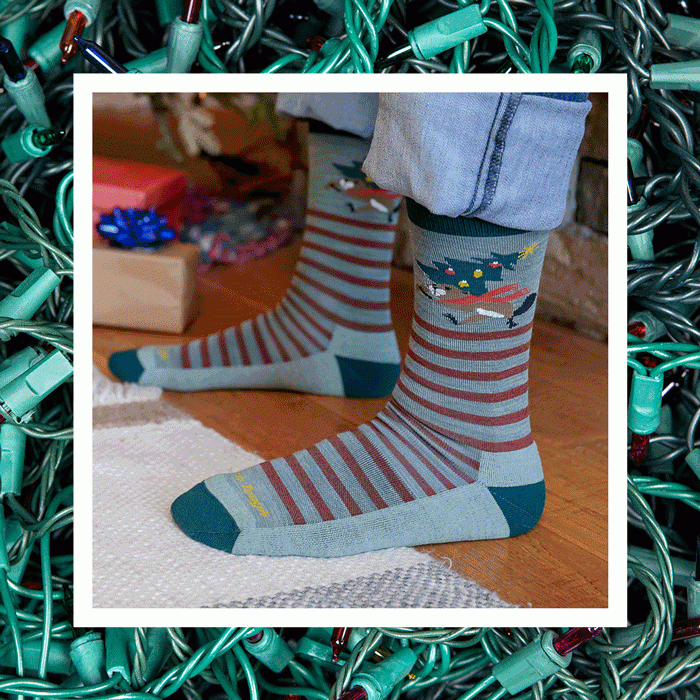 Shop Holiday socks - feet wearing red, white and green holiday socks pose in front of an illuminated tree