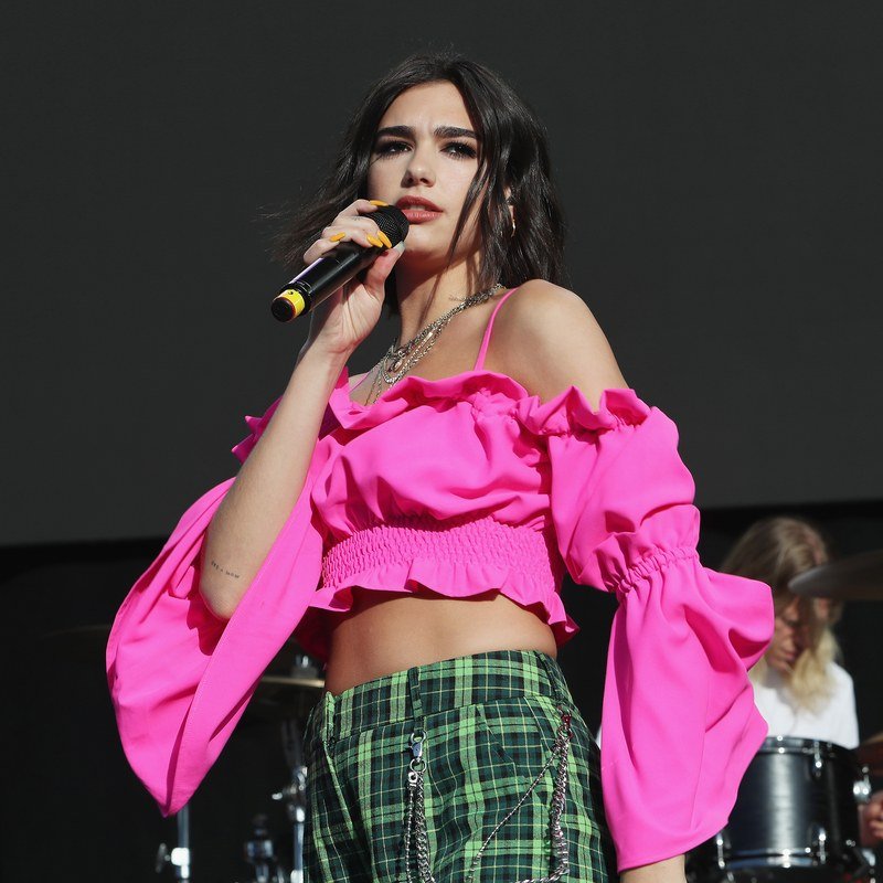 Dua Lipa performs onstage in a pink midriff baring top.