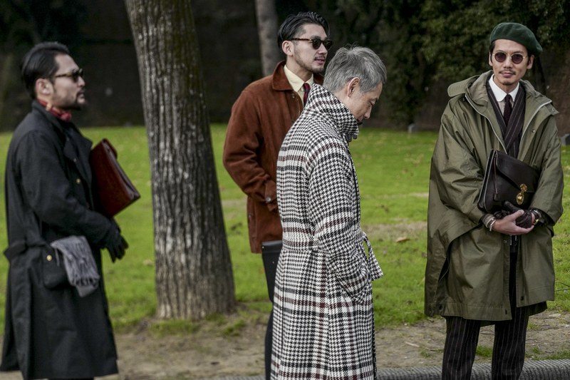 4 well-dressed men wearing fall coats standing next to a grassy patch