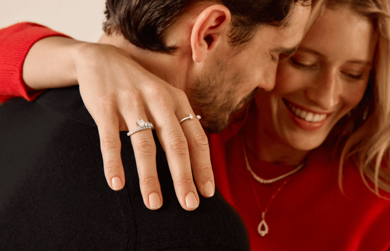 A woman embraces her male partner around his shoulders, showing off her stunning rings and necklaces