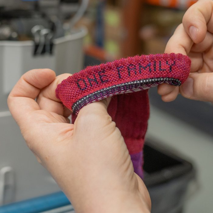 Learn More - the inside of a red sock cuff reads ONE FAMILY