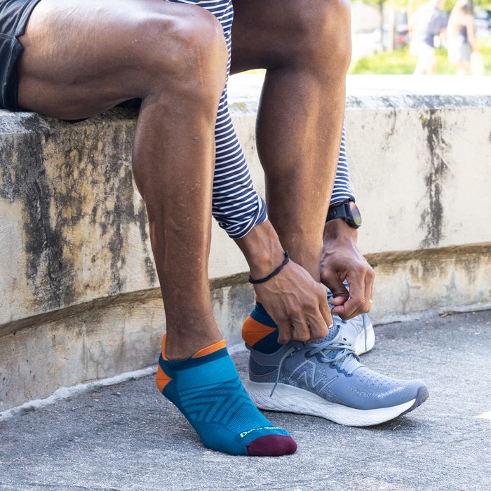 Runner seated and pulling on running sneakers over blue no show running socks from Darn Tough