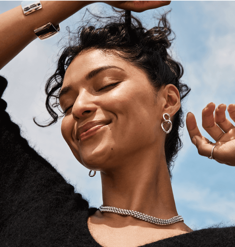 A smiling woman poses, showcasing her stunning necklaces, bracelets and earrings.