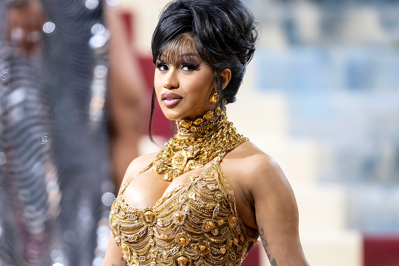 cardi b at met gala with a golden gown and large gold chains and updo 