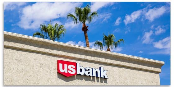 U.S. Bank logo on the front of a building, with a sunny sky and palm trees behind.