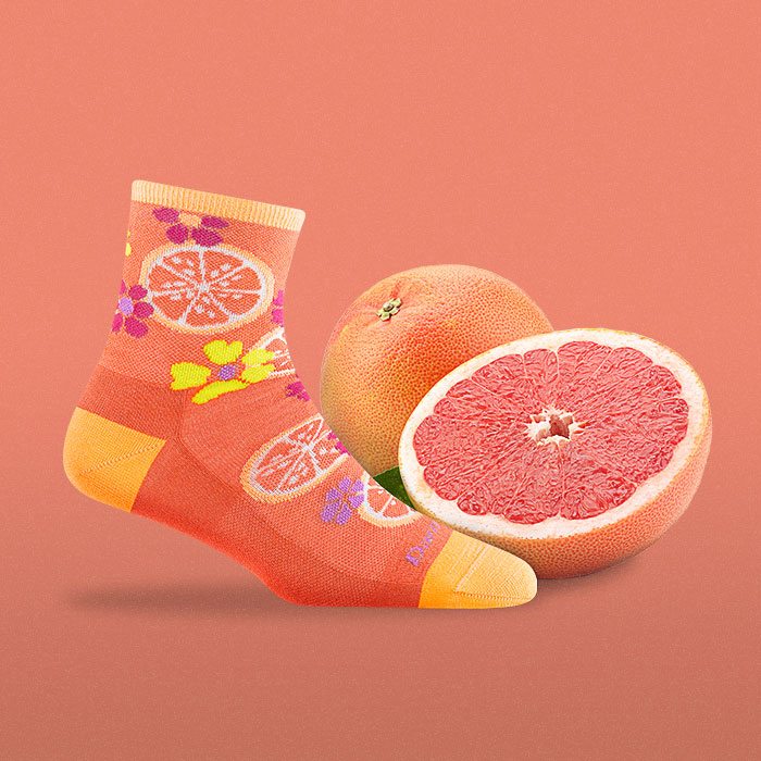 Shop Fruit Stand socks - an orange and yellow sock featuring grapefruits, next to an actual ruby red grapefruit