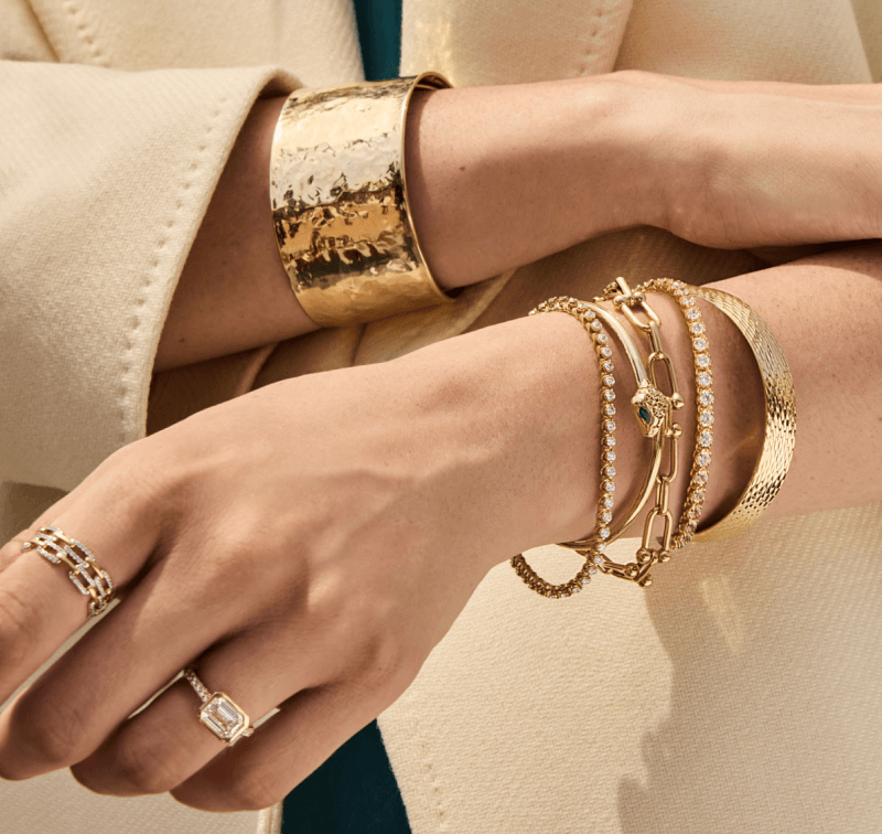 A woman wearing a red sweater rests her hand on her arm, showing off two stunning diamond rings