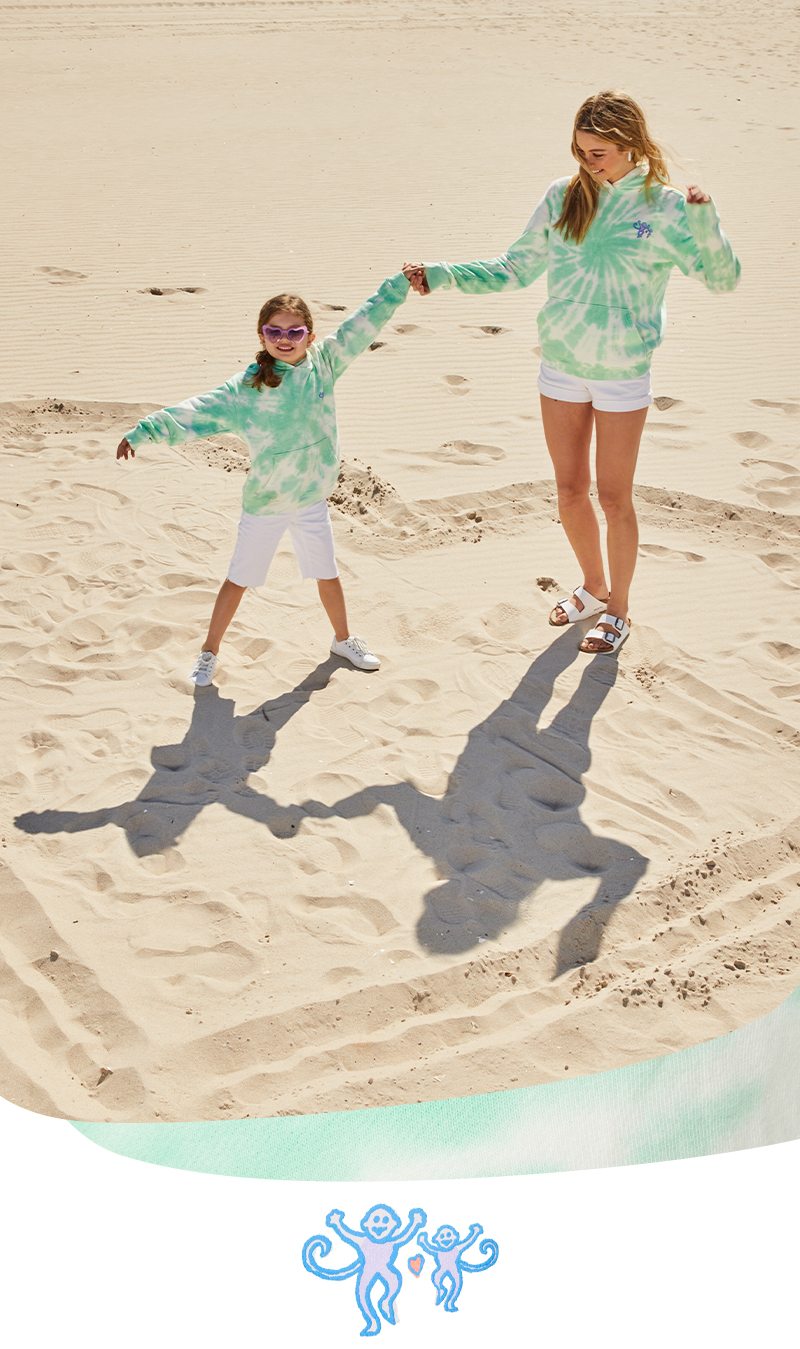Woman and little girl wearing the new Roller Rabbit Tie Dye Monkey Hoodies on the Beach with a heart in the sand