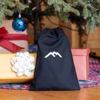 Gift bags now available - a black drawstring bag with Darn Tough's mountain logo sits under a tree