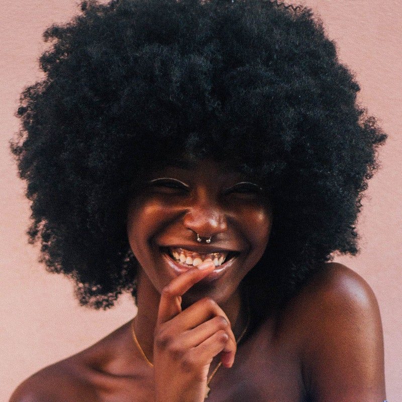 smiling woman with big fro in front of mauve pink background 