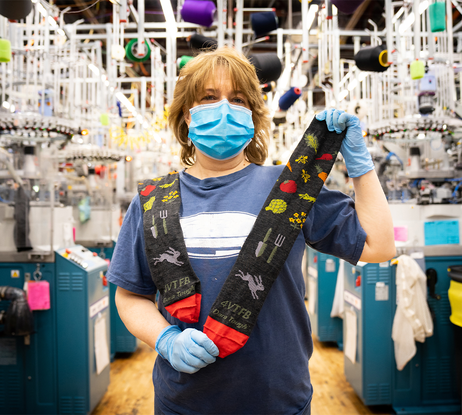 Amy holds the new Foodbank Farmer's Market sock as it comes off the knitting machine.