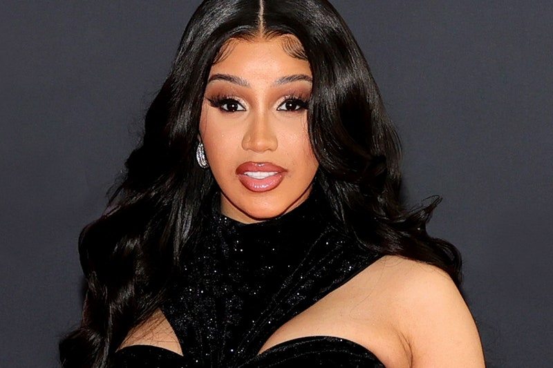Cardi B wearing a black dress with her hair down in front of a gray background