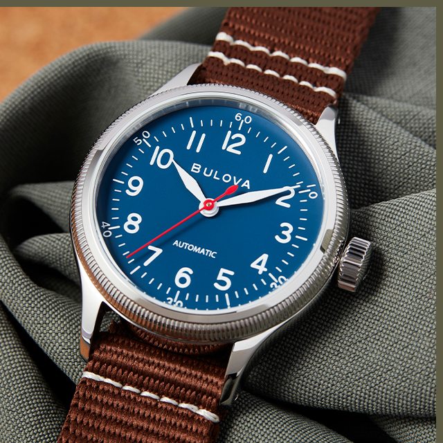 Close-up of silver-tone round case A-11 HACK watch with blue dial and brown nylon straps