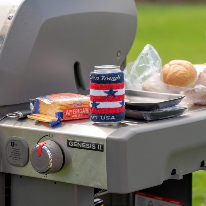 By the grill, a drink wrapped in an Americana Koozie, featuring red and white stripes and blue stars