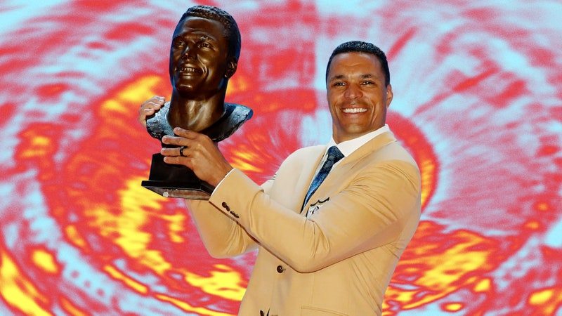 Tony Gonzalez holding his hall of fame bust on a psychedelic patterned background