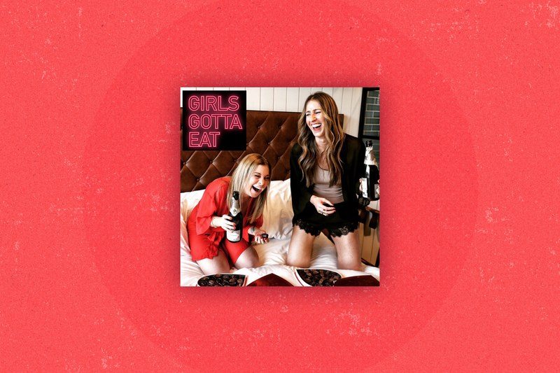 Podcast cover for GIRLS GOTTA EAT, showing two women with champagne and chocolates, laughing on a bed