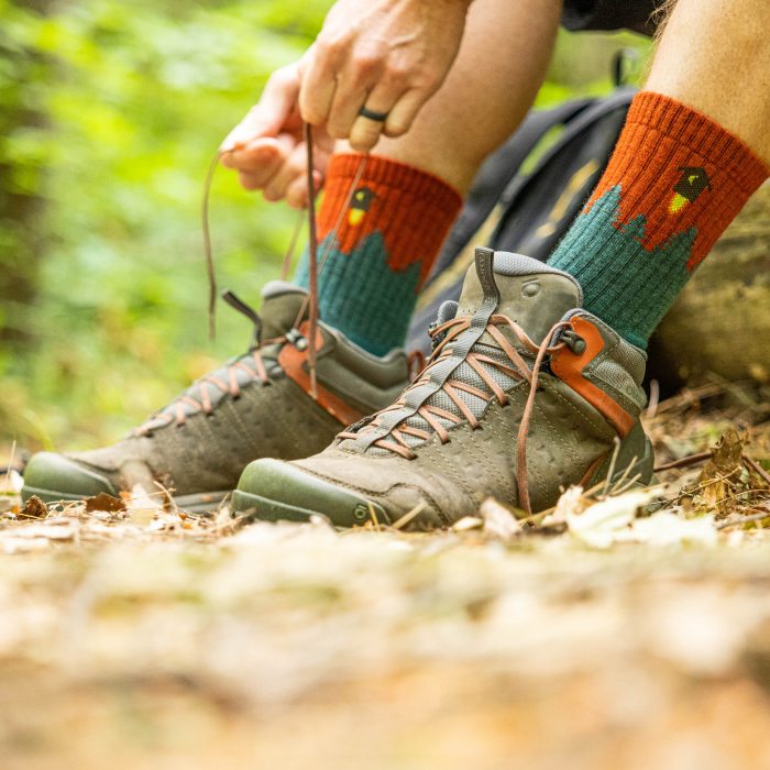 Hiker tying shoe laces and wearing the Number 2 sock with its rocket ship outhouse on full display