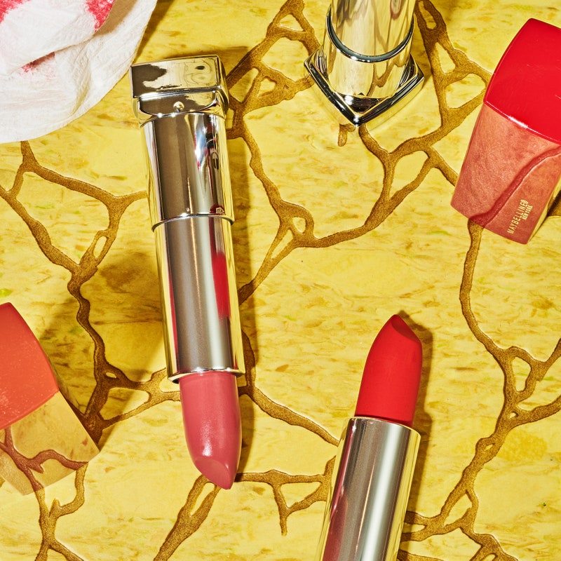 three open red lipstick tubes with caps off on a cracked yellow background