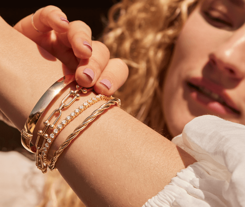 A smiling woman poses, adorned a variety of stunning Diamond & Gold Bracelets.