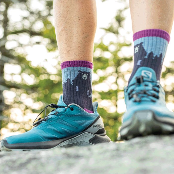 Shop Bear Town socks - a hiker stands on a rock wearing blue and purple bear-patterned socks