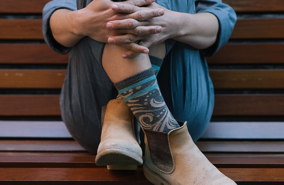 A woman (maybe a mom?) sitting on a bench entwines her fingers around her calves, pulls her legs close to her chest, shows off her whimsically designed socks.