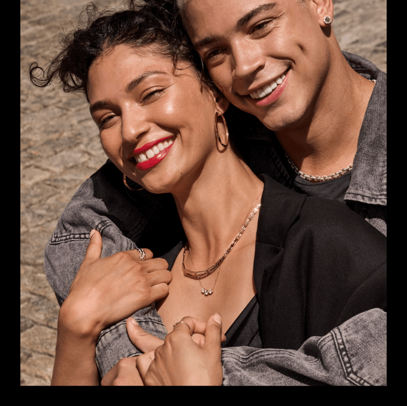 A smiling couple poses, adorned with beautiful Necklaces, Rings, Bracelets, & Earrings.