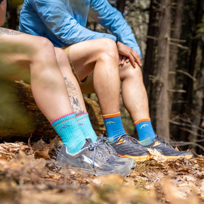 Shop Limited Edition Socks - two hikers sit on a log in the woods, wearing bright blue Darn Tough hiking socks.