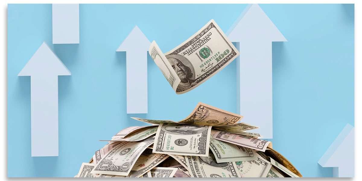 A pile of money with a single hundred-dollar bill falling on it, in front of white up-arrows on a blue background.