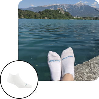 read the blog - View of someone relaxing by an alpine lake with mountains in the background, wearing white low-cut socks.