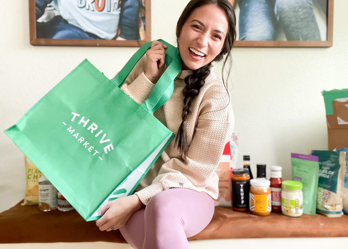 woman holding green thrive market bag with groceries on bench