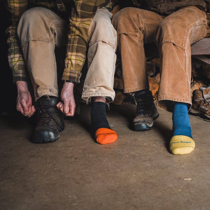Shop Work Socks - two sugarers sit on a bench, both wearing Steely work socks, in black and orange, and blue and yellow
