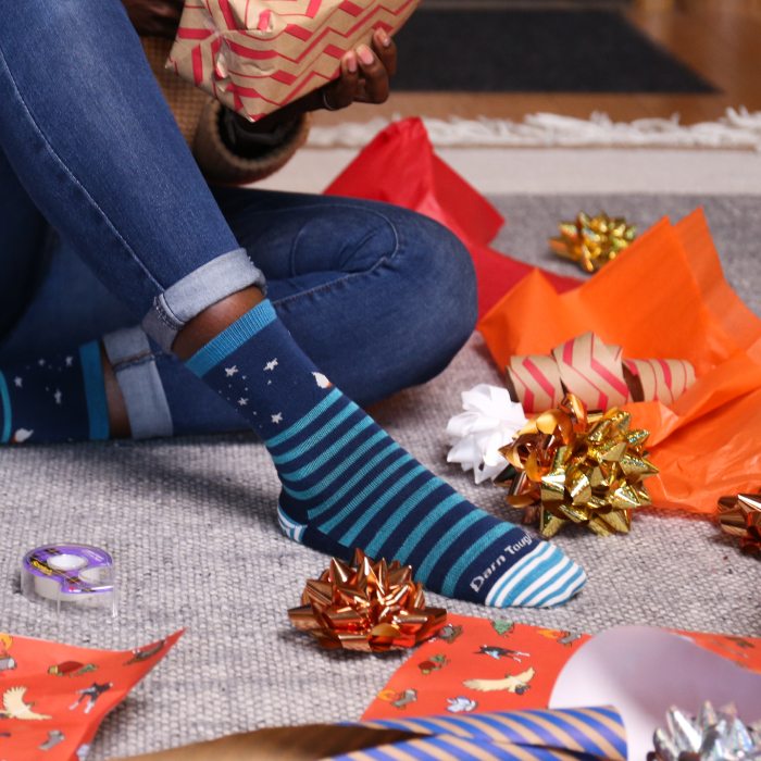 Shop the Gift Guide - sitting on the floor surrounded by bows and paper, a gift-wrapper wears blue striped socks