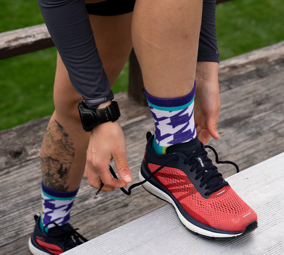 A runner laces up their shoes on the bleachers while flashing bright and stylish socks for the world to see.