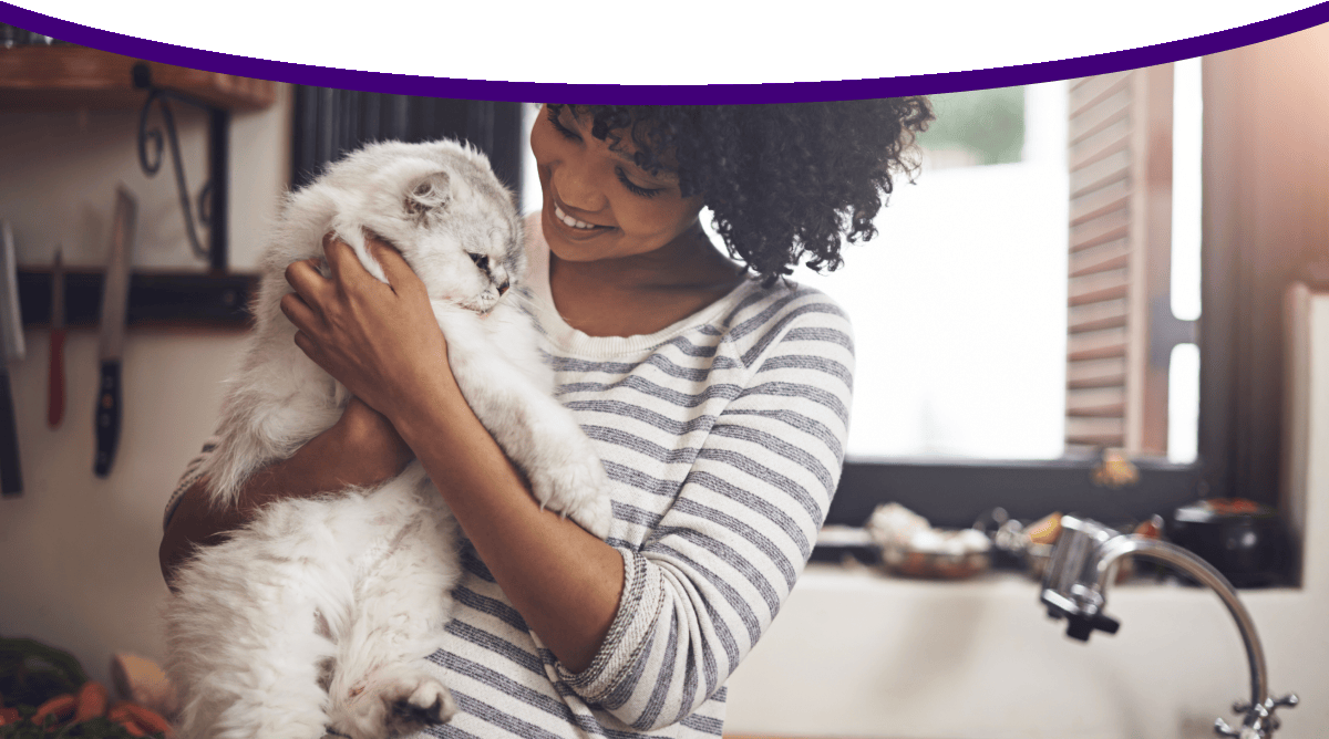 A woman smiles at the long-haired white cat she is holding. 