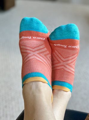 A pair of feet wearing orange and blue no-show running socks from Darn Tough