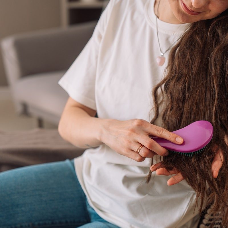 A girl combs her brown wavy hair with a purple comb.