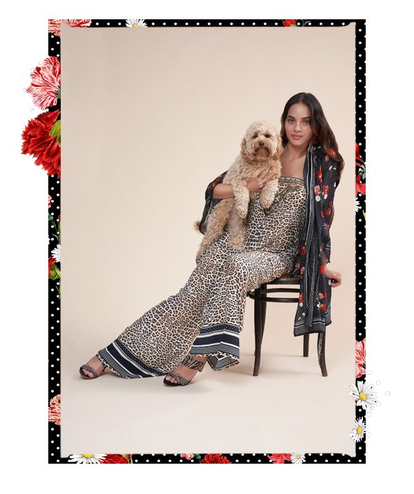 Model wearing leopard print jumpsuit with dress as a layer, holding puppy.