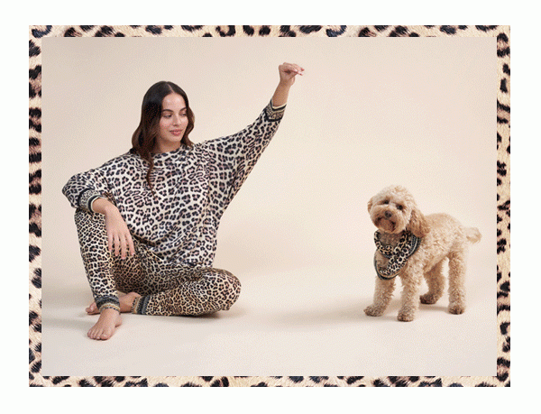 Model wearing leopard print jumper and pants playing with puppy.